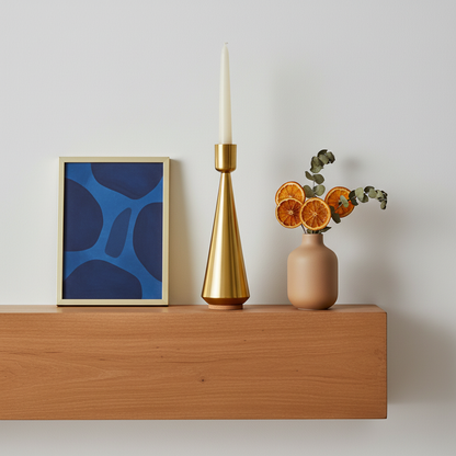 Gold-tone tapered candle holder styled on a terracotta mantel with cobalt artwork and dried stems