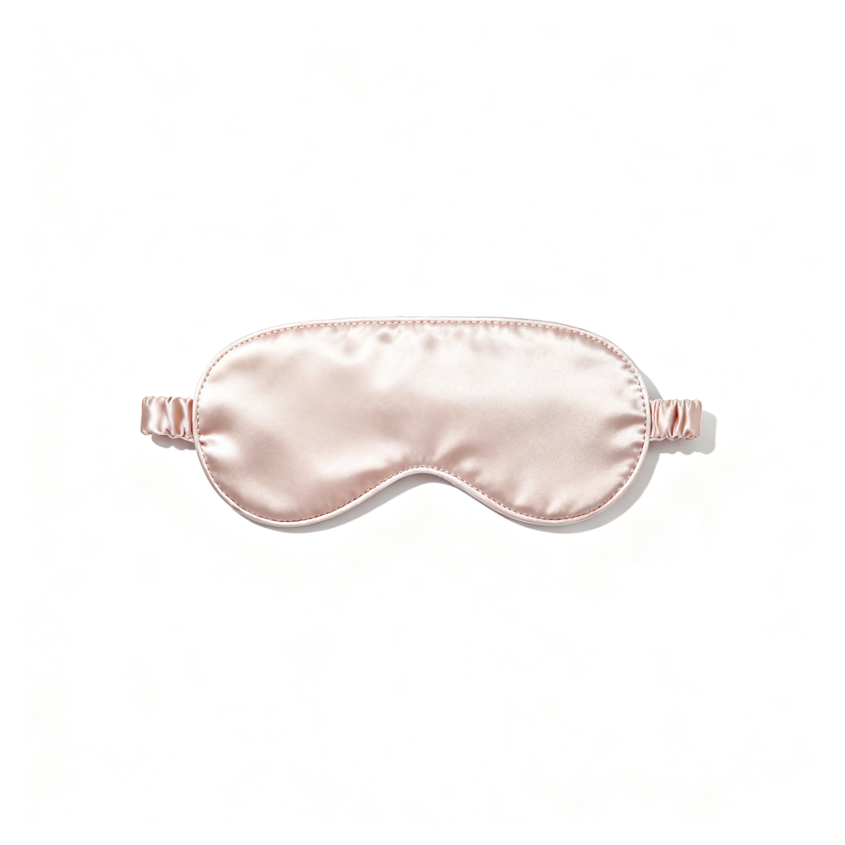 Blush-pink satin sleep mask with softly padded curved shape on a white background